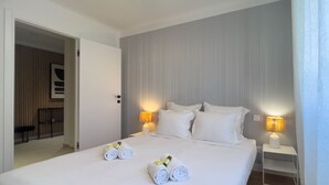 A hotel room with a neatly made bed, two bedside lamps, and a view of a wooden room through an open door. - LE ROSSINI Antibes Center, AirCo, Parking for 4 By Sunset (Antibes)