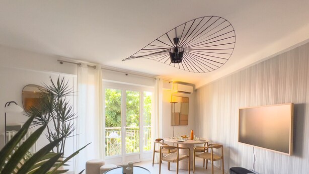 A modern living room with a round dining table, chairs, a TV mounted on the wall, and a large window with curtains. - LE ROSSINI Antibes Center, AirCo, Parking for 4 By Sunset (Antibes)