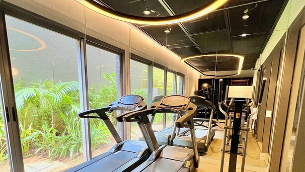 A gym with treadmills and exercise equipment, large windows with a view of greenery, and a modern ceiling design. - AD 330 (São Paulo)