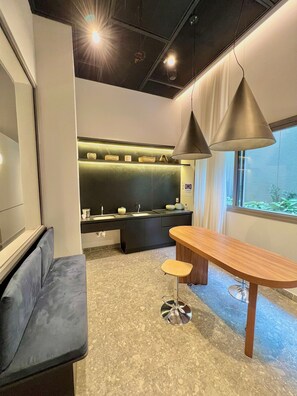 A modern kitchen with a black countertop, a built-in sink, and a green backsplash. There is a wooden dining table with two stools and a pendant light above it. - AD 330 (São Paulo)