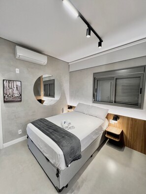 A modern bedroom with a bed, bedside tables, a mirror, and a window with blinds. - AD 330 (São Paulo)