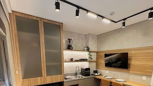 A compact hotel room with a bed, a desk, a kitchenette, and a TV mounted on the wall. - AD 330 (São Paulo)