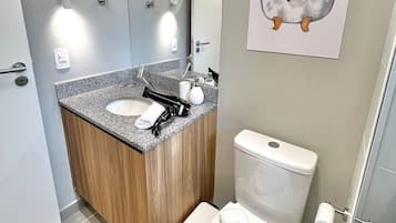 Un baño moderno con lavamanos de granito, tocador de madera, inodoro blanco y espejo montado en la pared.