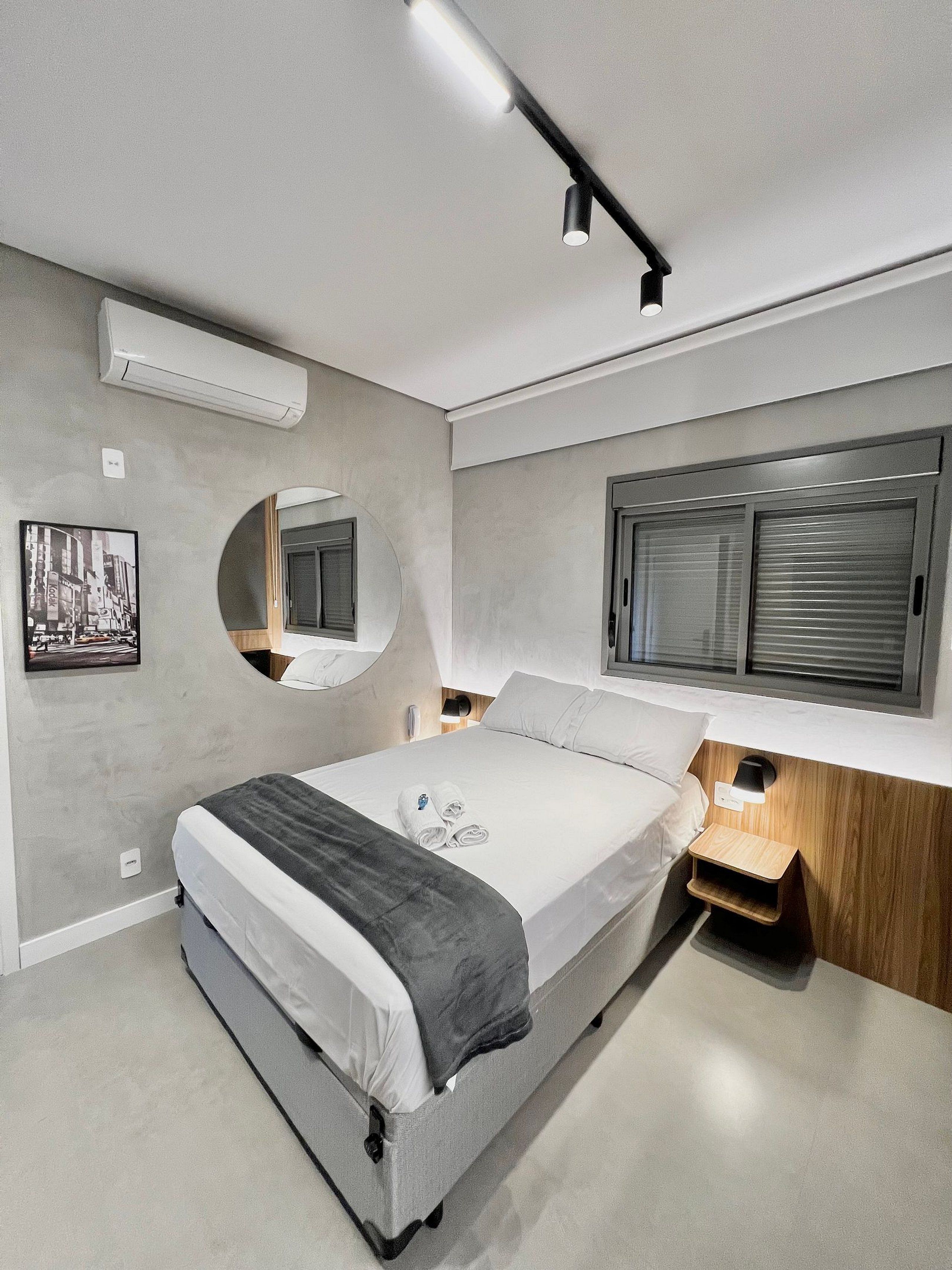 Un dormitorio moderno con cama, mesitas de noche, un espejo y una ventana con persianas.