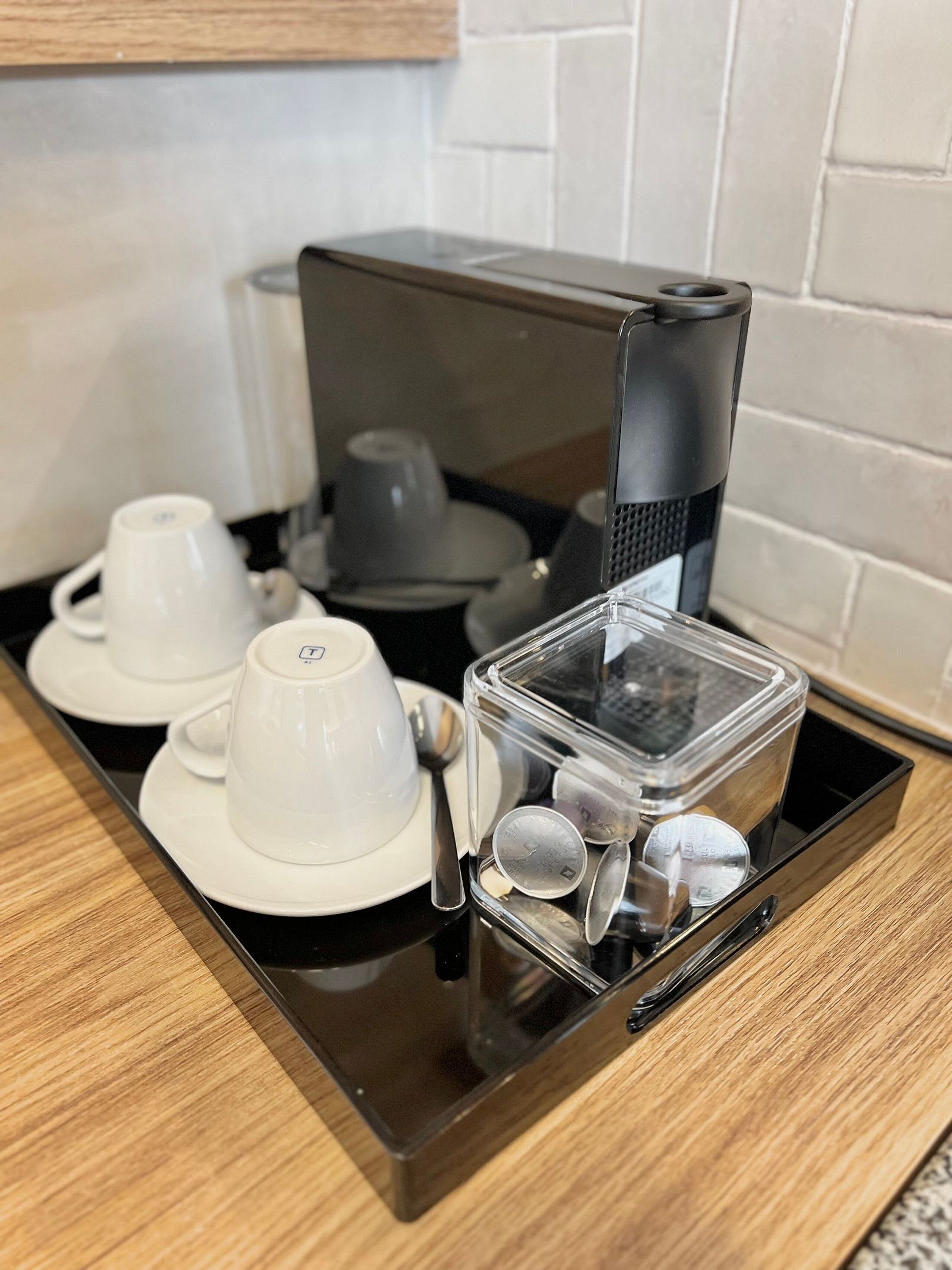 A coffee maker on a black countertop with white cups and a spoon.