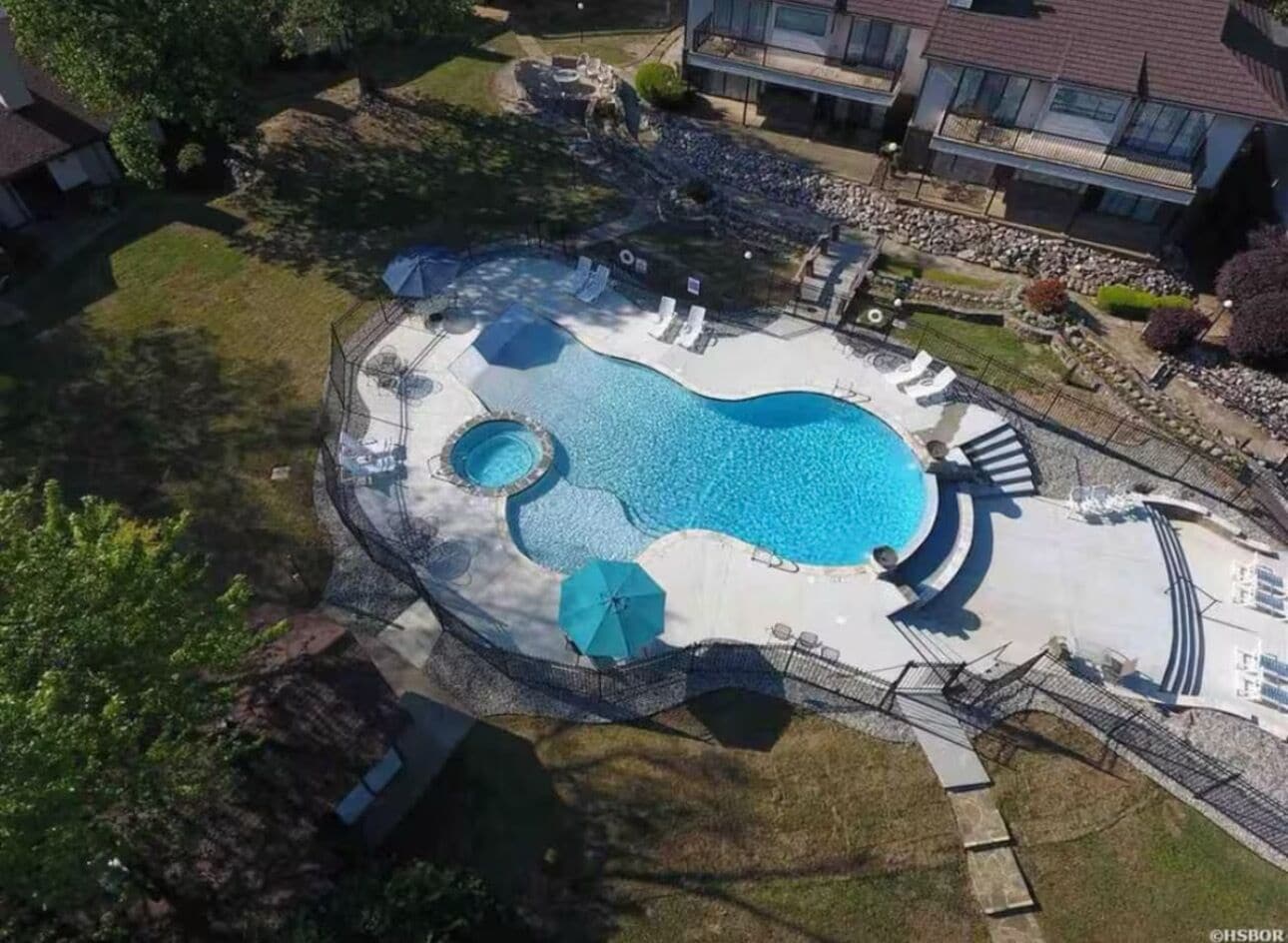 Vista aérea de uma área residencial com piscina, cadeiras de descanso e guarda-sóis.