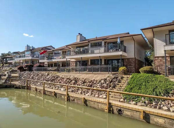 A waterfront property with multiple balconies, a stone retaining wall, and a clear view of the water.
