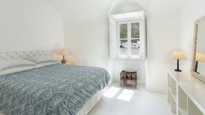 Un dormitorio con cama, ventana, una mesita y un espejo.