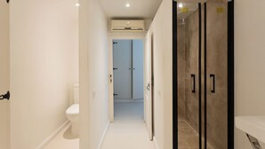 Un pasillo estrecho que conduce a un baño con inodoro, zona de ducha y una puerta con diseño geométrico.