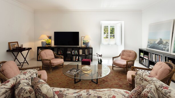 Un salón con dos sillones de mimbre, una mesa de centro de vidrio, una estantería y un televisor de pantalla plana.