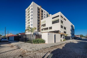 Un edificio moderno de varios pisos con fachada plana, entrada protegida por una reja y una calle pavimentada al frente.