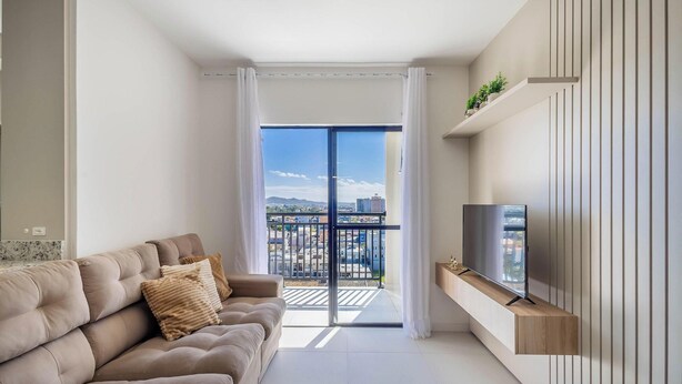 Un salon moderne avec un canapé, un téléviseur à écran plat et un balcon offrant une vue sur la ville.
