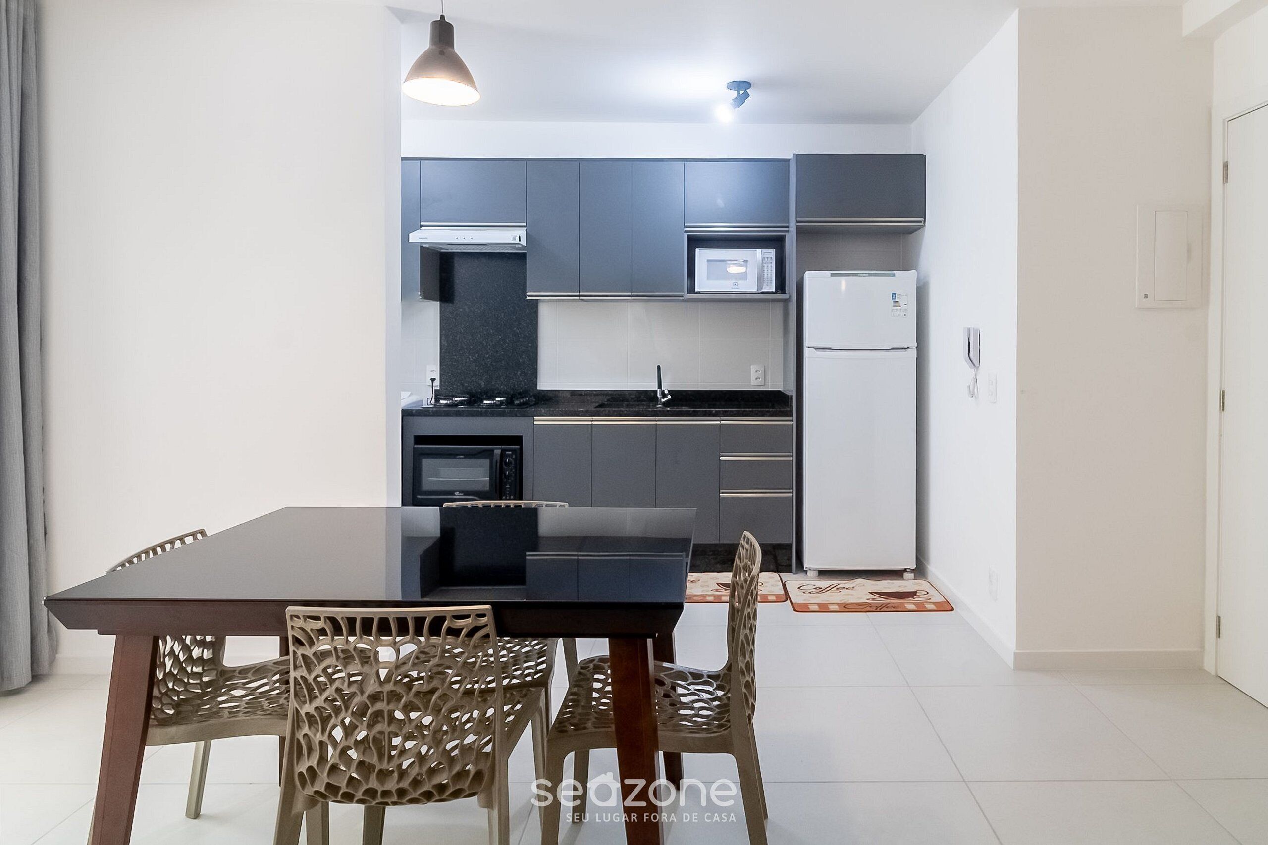 A modern kitchen with grey cabinets, a black countertop, and a white refrigerator. There is a dining table with chairs in the foreground.