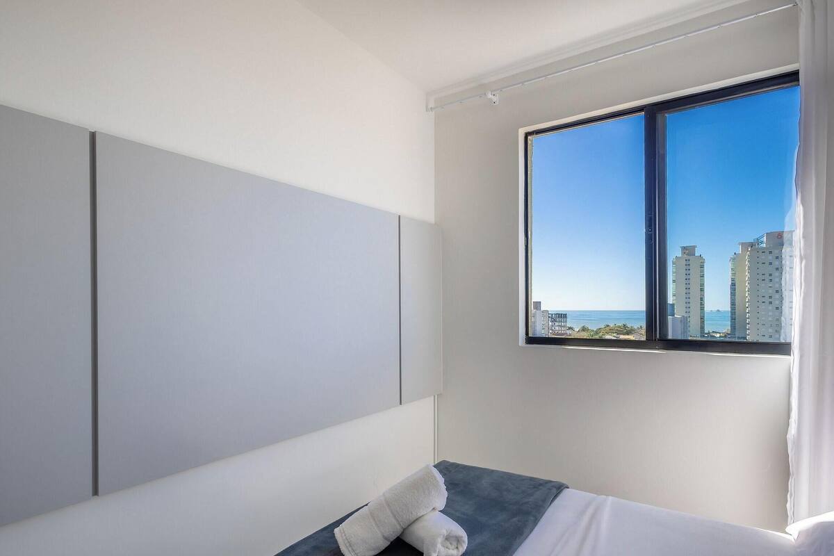 A hotel room with a large window, a bed, and a wardrobe.