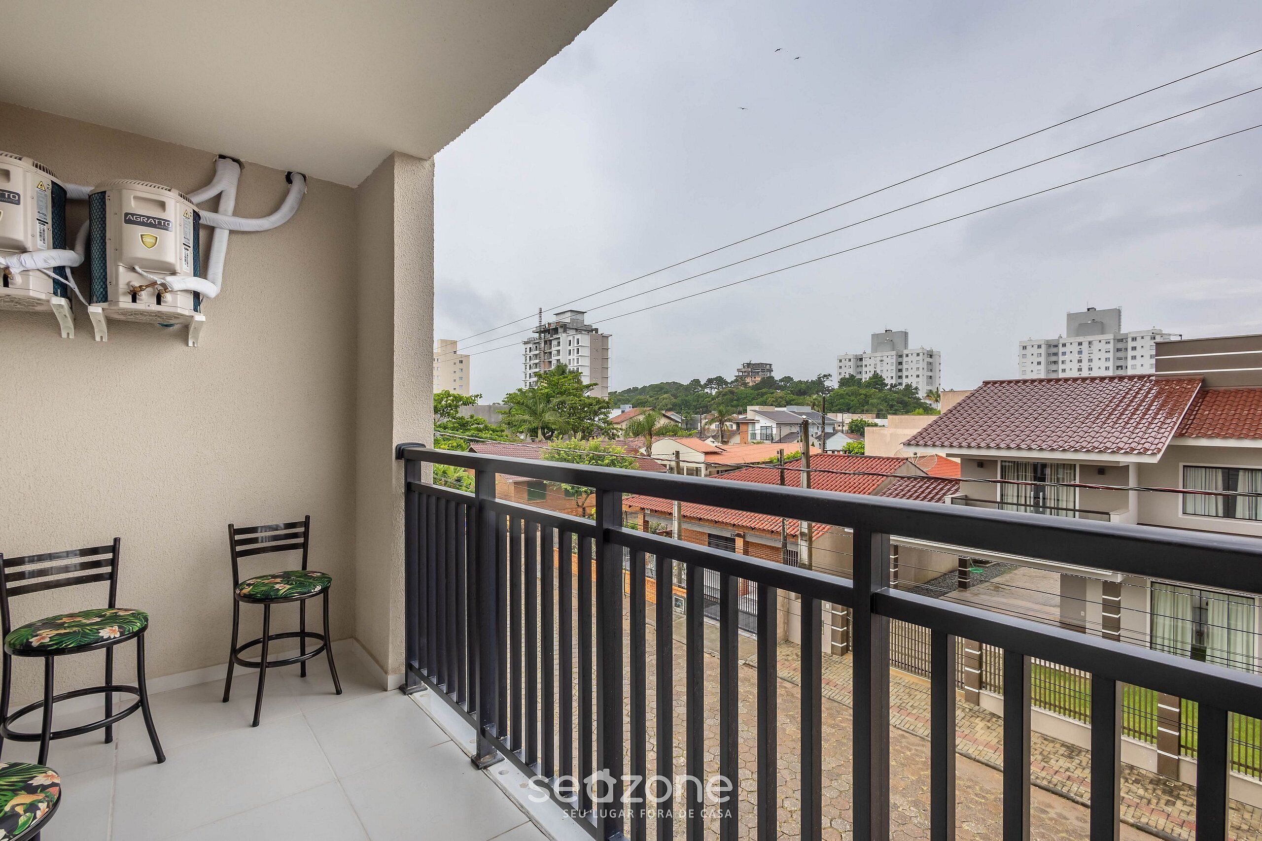 A balcony with two chairs, a water heater, and a view of a cityscape.