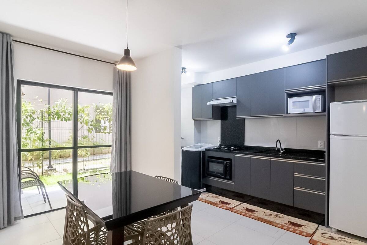 A modern kitchen with dark cabinetry, a microwave, a refrigerator, and a dining area with a table and chairs.