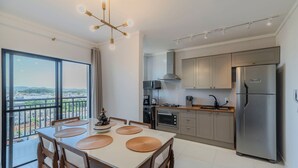 Une cuisine moderne dotée d’une grande fenêtre, un coin repas avec une table et des chaises, et un balcon offrant une vue sur la ville.