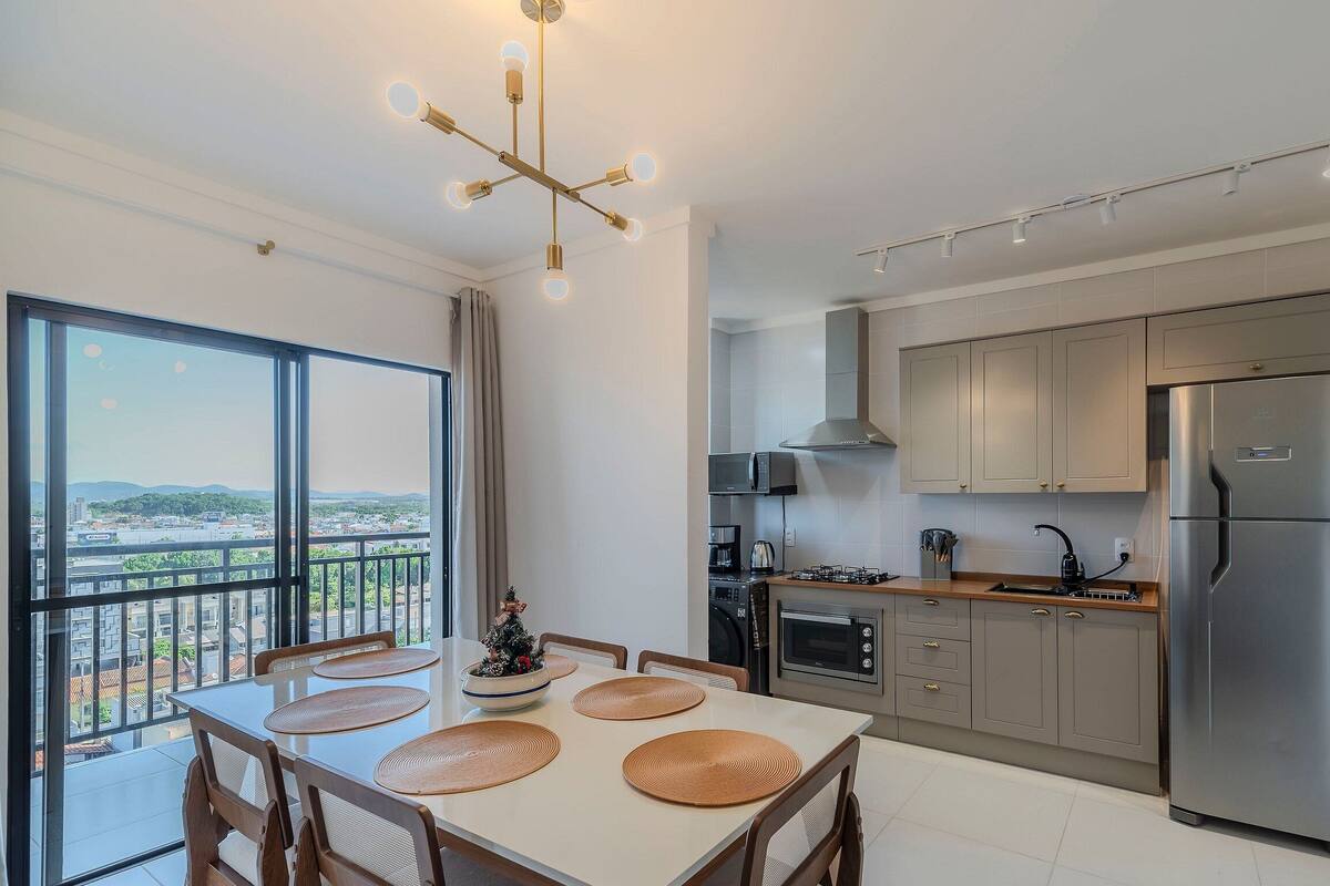 A modern kitchen with a large window, a dining area with a table and chairs, and a balcony with a view of the city.