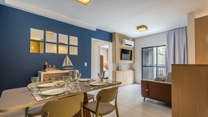 Un espace repas moderne avec une table dressée pour quatre personnes, un téléviseur fixé au mur et une vue sur l’extérieur par une fenêtre.