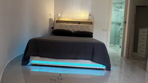A modern bedroom with a bed, a nightstand, and a bathroom visible in the background.