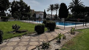 A swimming pool surrounded by a fence, with a clear sky and greenery in the background.