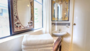 A bathroom with a large mirror, a sink, and a stack of white towels on a wooden bench. - Cozy 10-bedroom bungalow in Cameron Highlands (Tanah Rata)