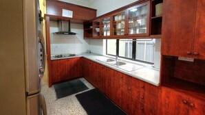 A kitchen with wooden cabinets, a stainless steel refrigerator, and a window above the sink. - Cozy 10-bedroom bungalow in Cameron Highlands (Tanah Rata)