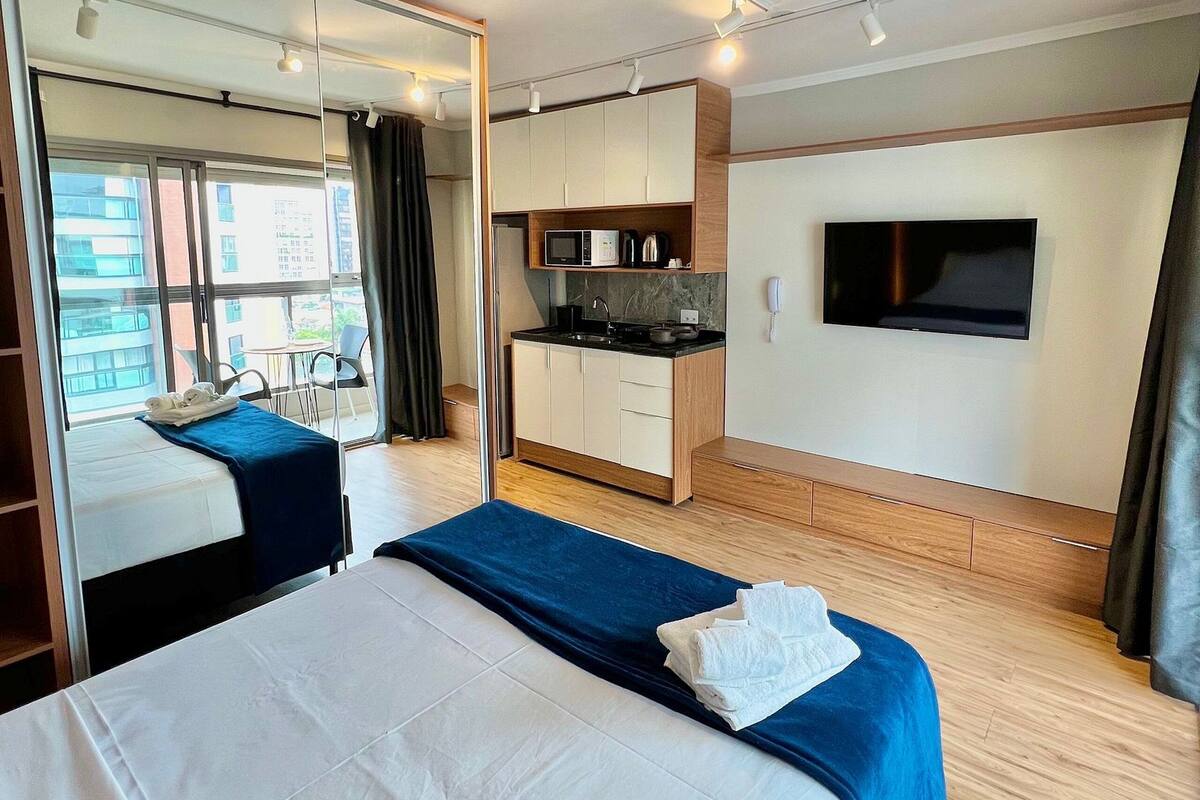 Une chambre d’hôtel avec un lit, une petite kitchenette, une télévision et un grand miroir.