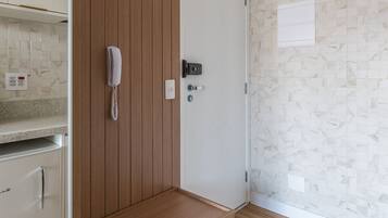 Ett rum med en väggpanel av trä, en vit dörr, en telefon och en liten hylla.