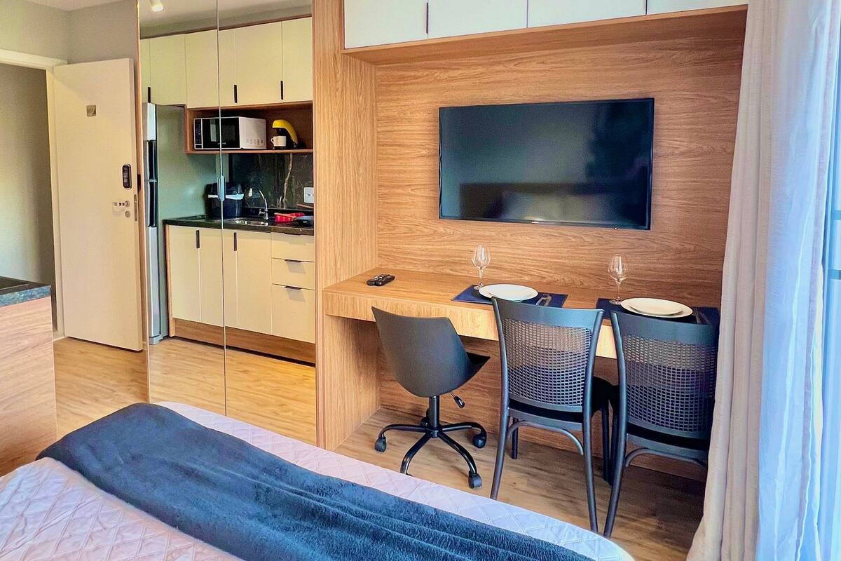 Une chambre d’hôtel moderne équipée d’un lit, d’un bureau avec deux chaises, d’un téléviseur à écran plat, d’un four à micro-ondes et d’une kitchenette.