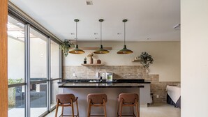 Una cocina moderna con una isla grande, taburetes de bar, lámparas colgantes y vistas amplias a través de ventanas.