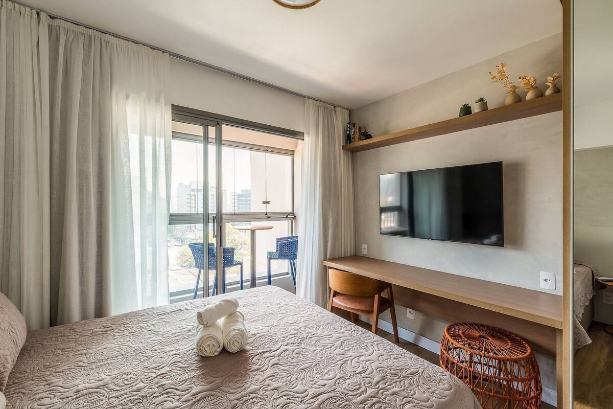 Une chambre d’hôtel avec un lit, un bureau, une télévision et un balcon équipé de chaises.