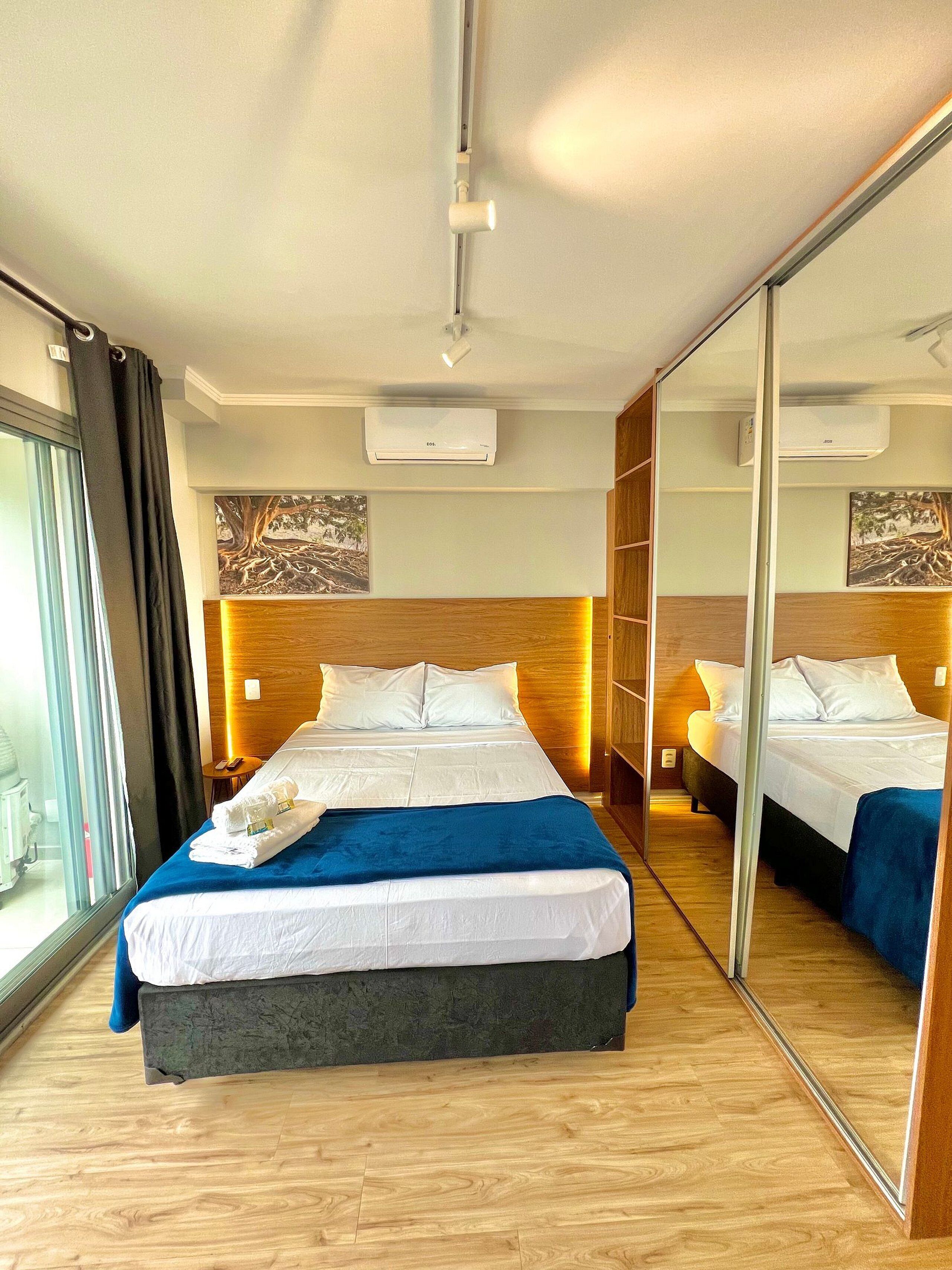 A hotel room with a large bed, a mirror, and a view of the outside.