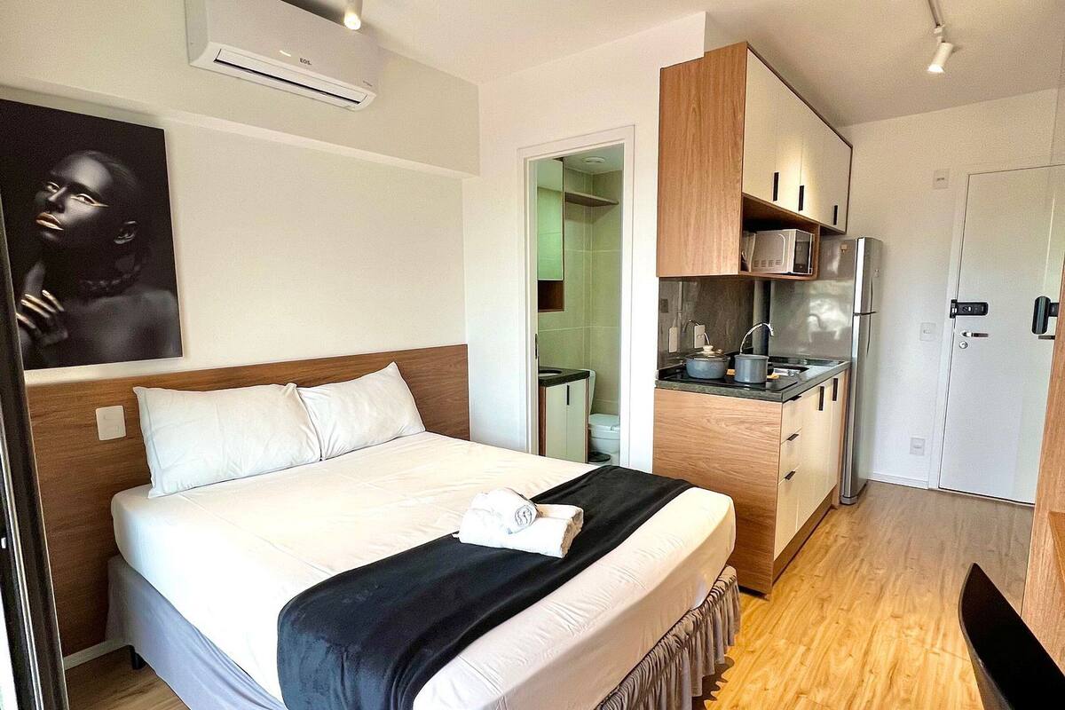 Une chambre d’hôtel moderne dotée d’un grand lit, d’une kitchenette et d’une salle de bain visible à travers une porte ouverte.