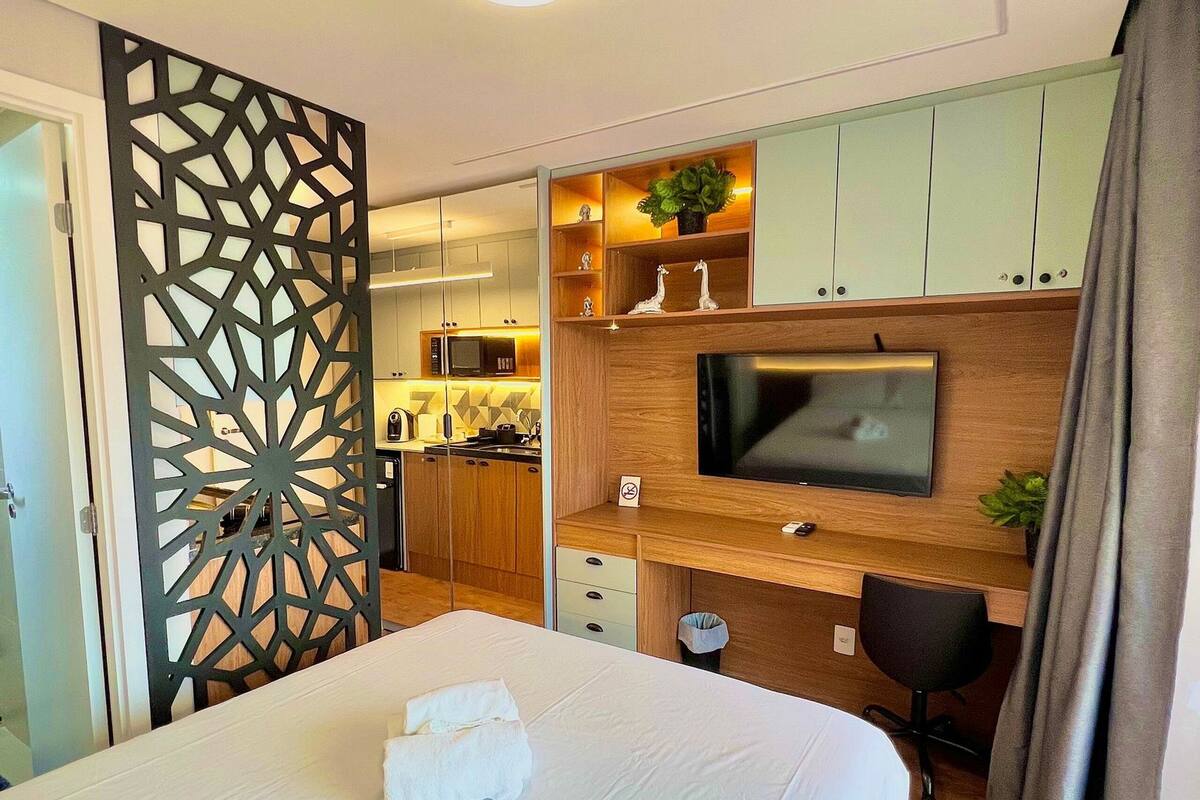 Une chambre d’hôtel comprenant un lit, une télévision, un bureau, une chaise, un coin cuisine et un élément de séparation décoratif.