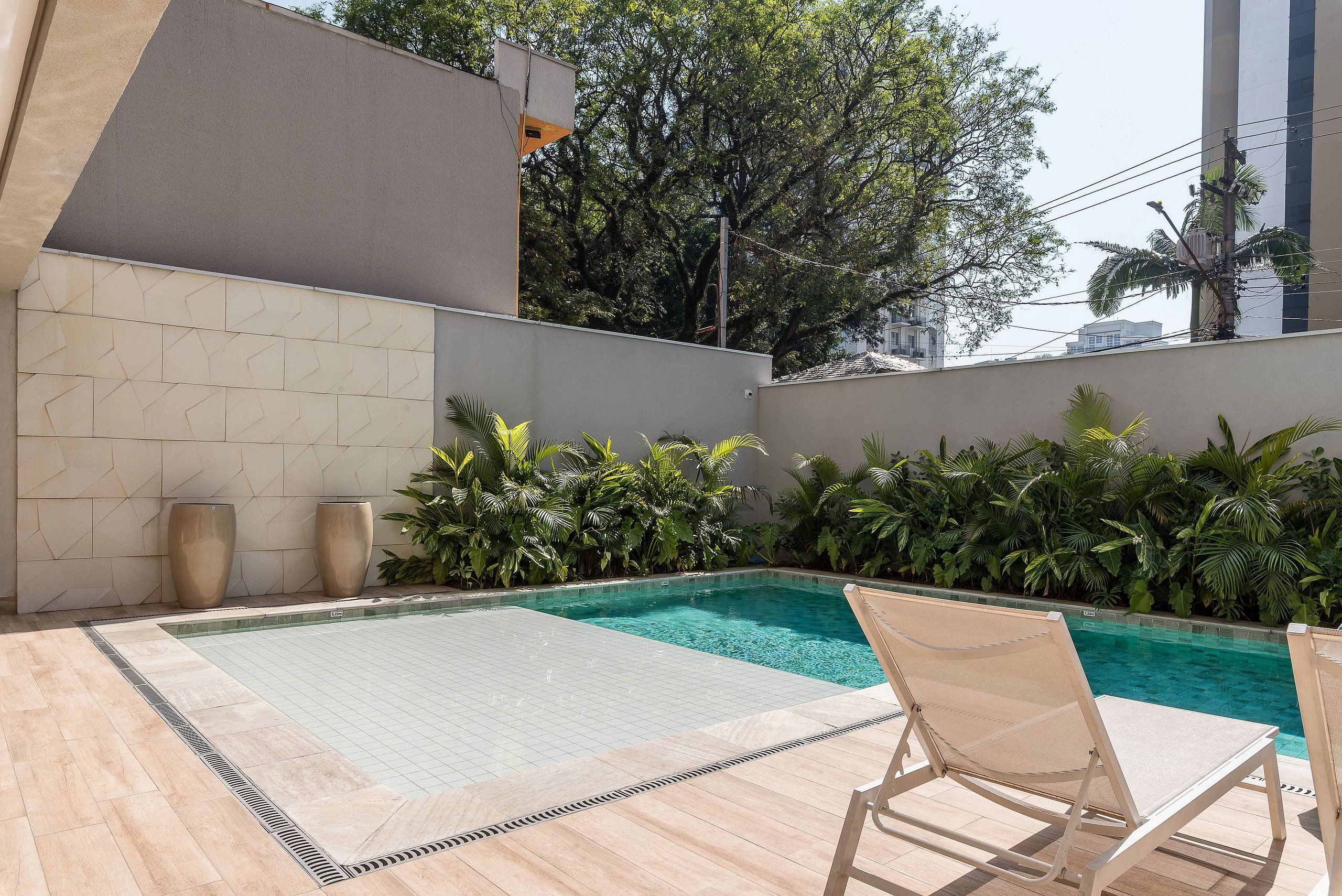 Une piscine dont les bords sont recouverts de carreaux, deux chaises longues et une terrasse également recouverte de carreaux.