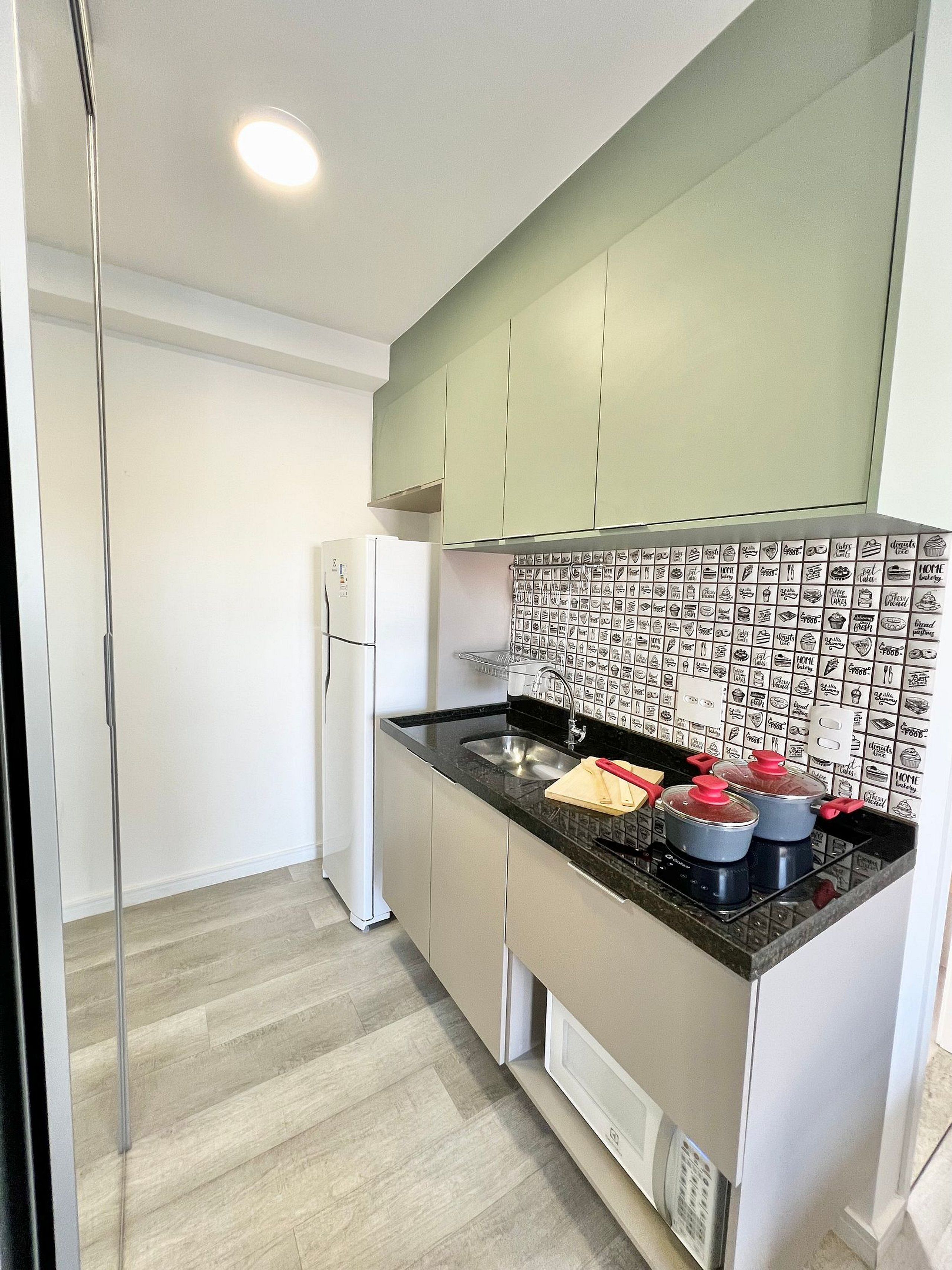 A modern kitchen with a refrigerator, a sink, and a backsplash with food illustrations.