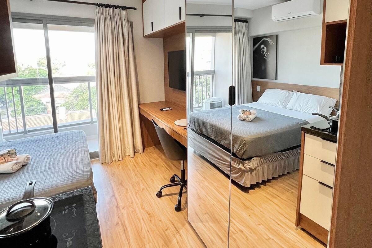 Une chambre d’hôtel moderne dotée d’un grand lit, d’un bureau, d’un miroir et d’un balcon avec des rideaux.