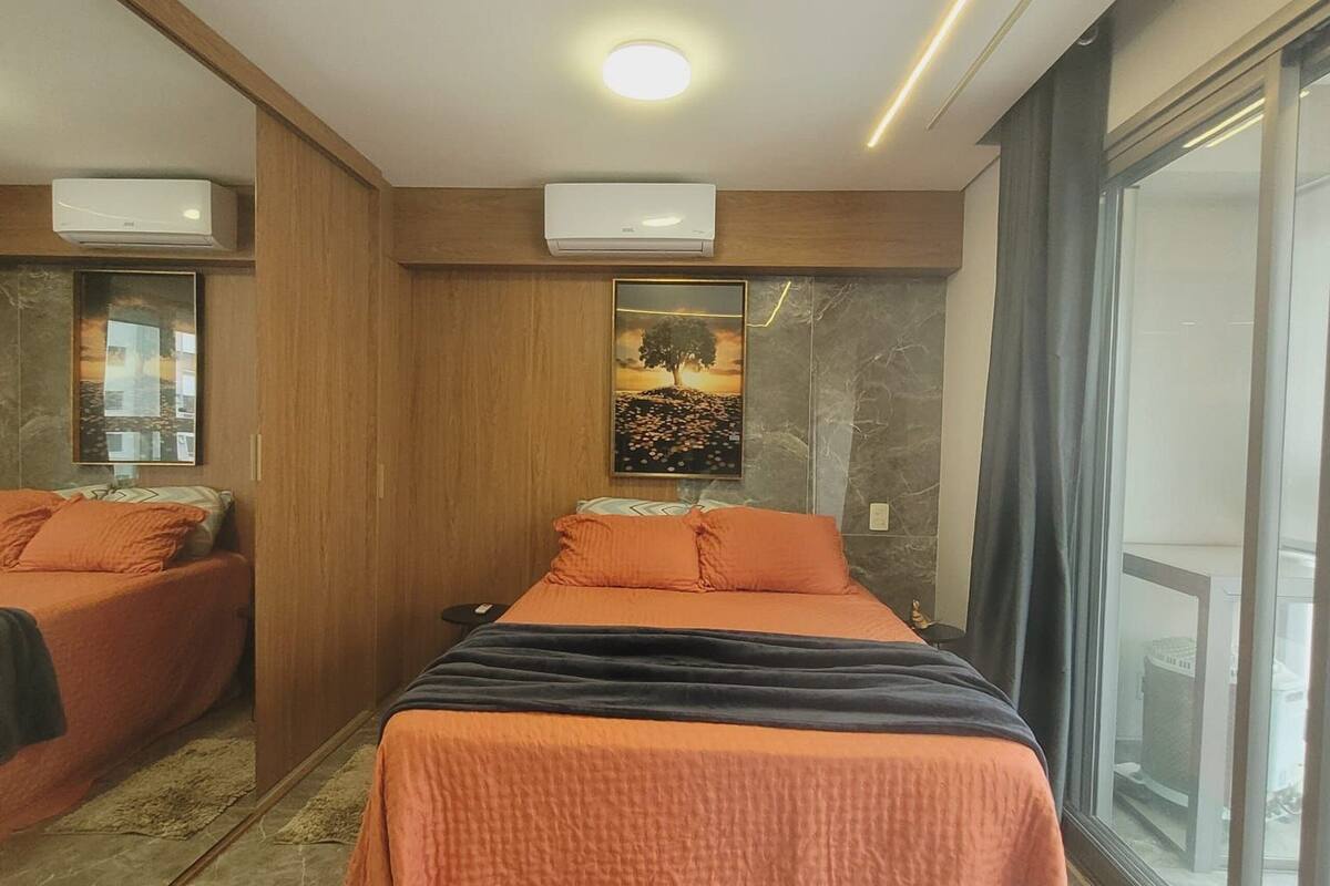 Une chambre moderne avec un lit, deux tables de chevet, un climatiseur fixé au mur, une grande fenêtre et un sol en marbre.