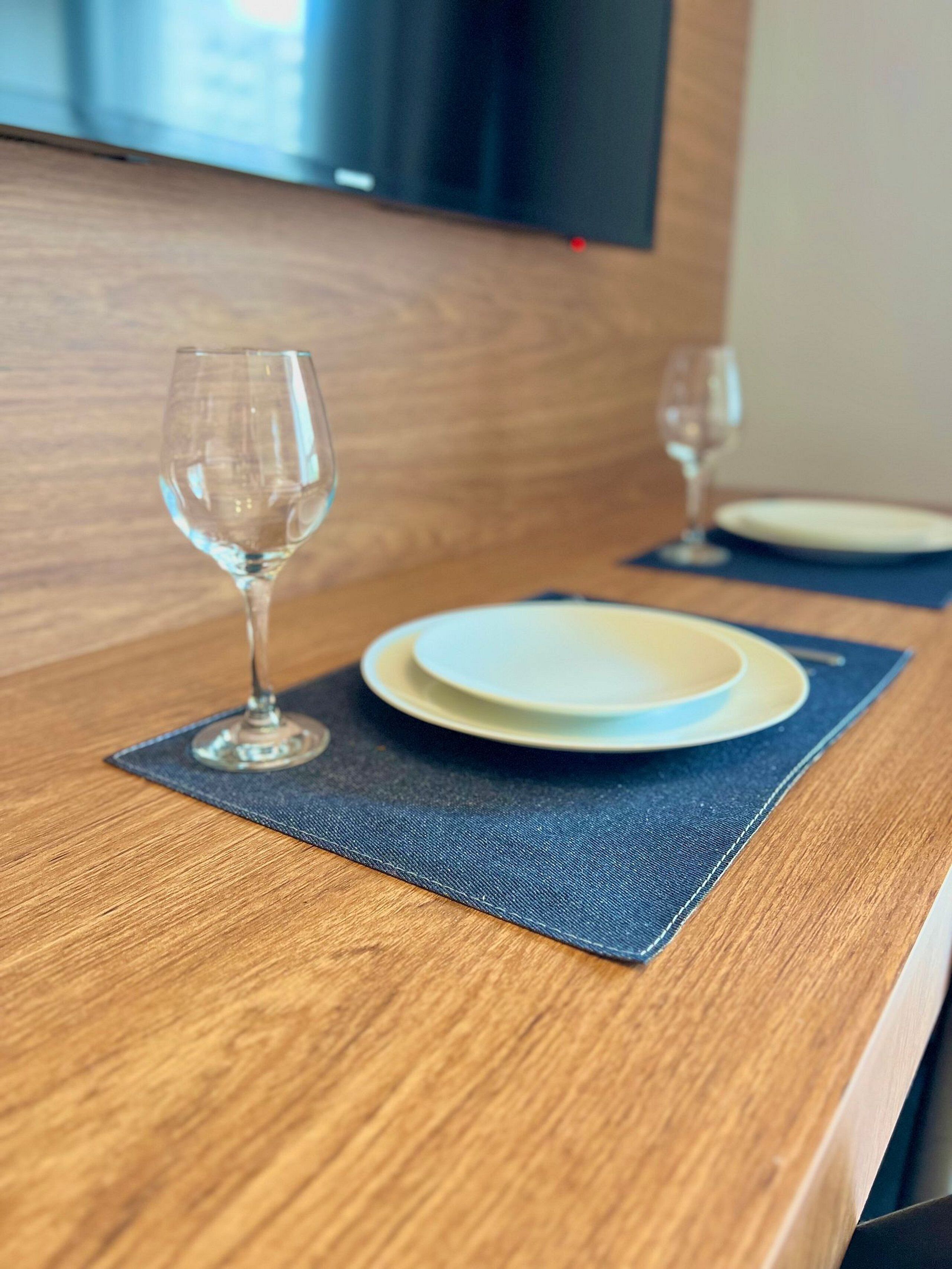 A wooden table with a blue placemat, a white plate, and a wine glass.
