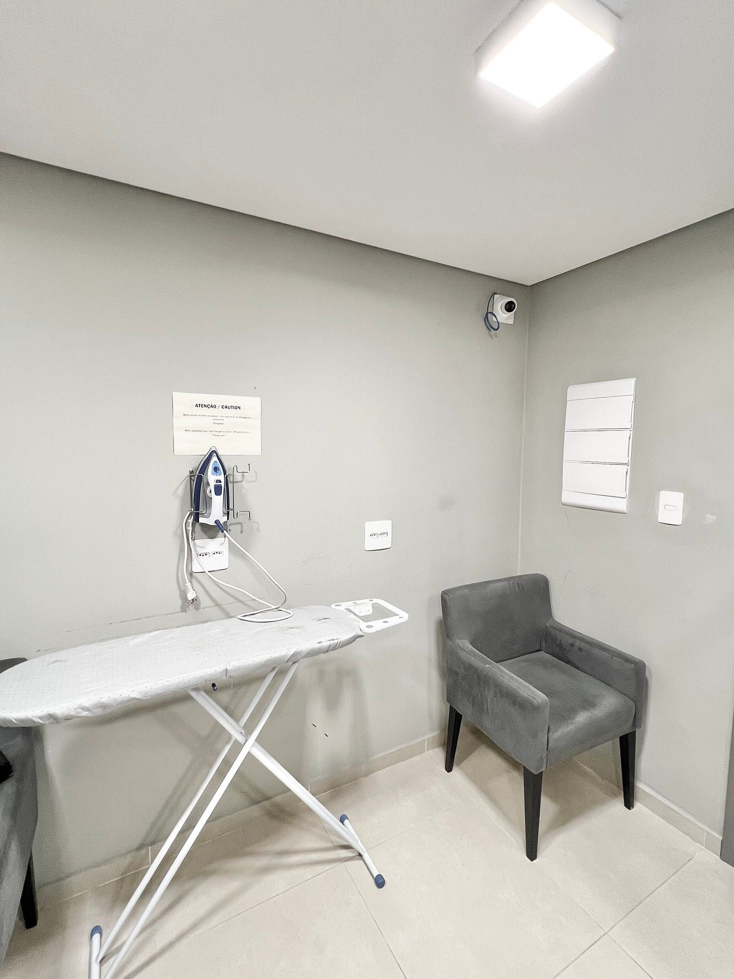 A room with a flat iron, a chair, a wall-mounted camera, and a caution sign.