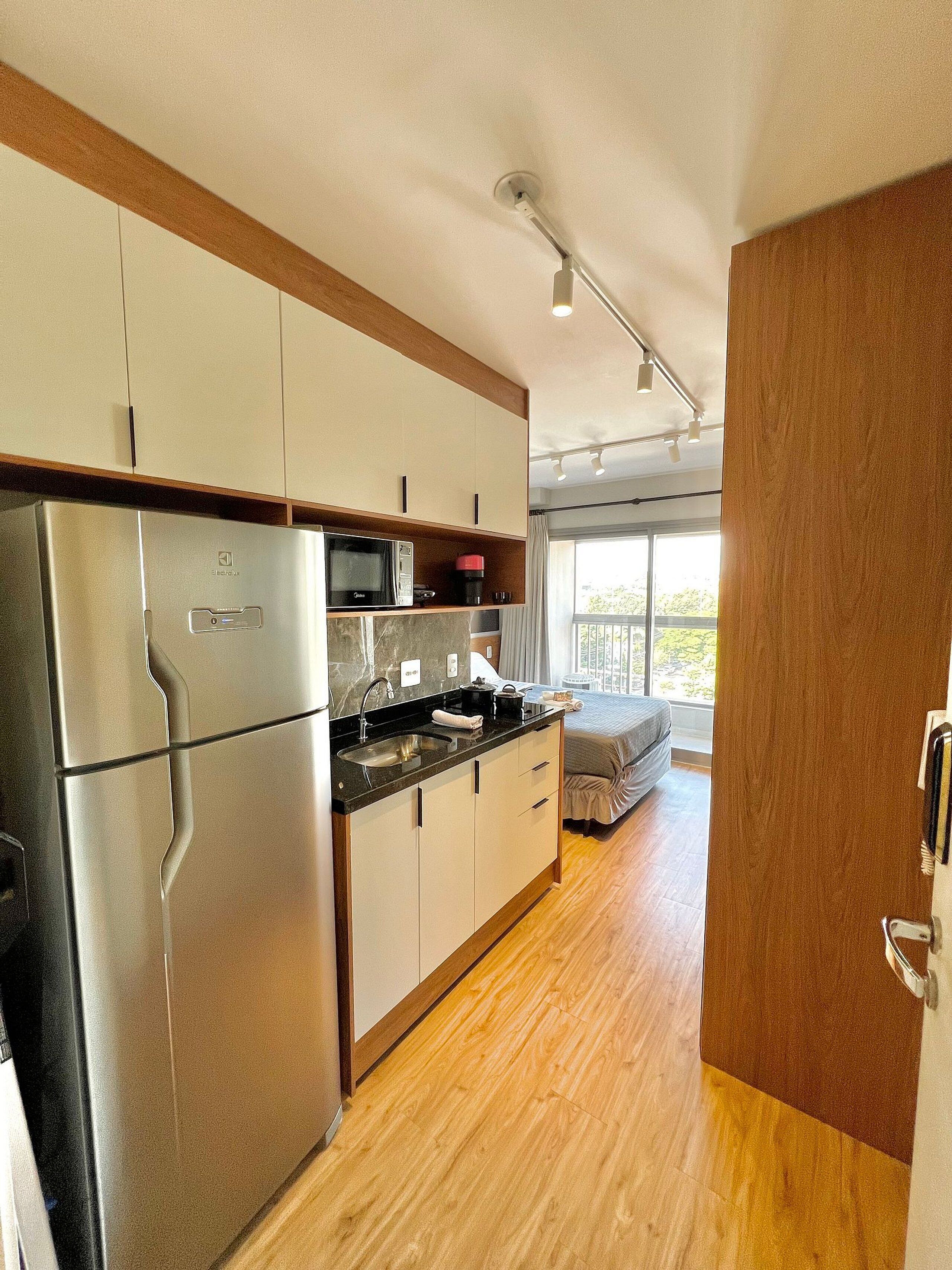 A compact kitchen with modern appliances, a dining area with a sofa, and a large window providing natural light.