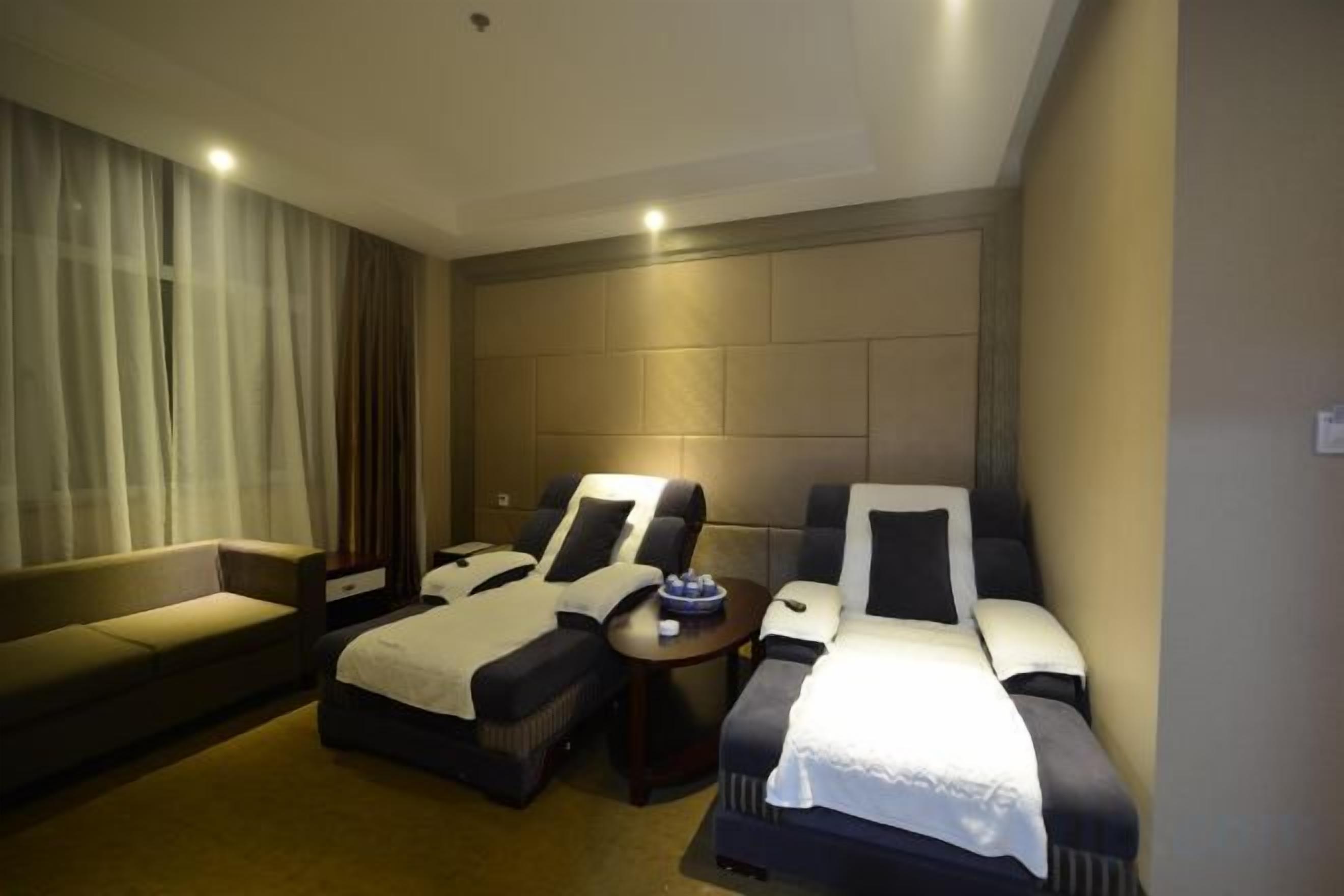 A hotel room with two beds, a sofa, a massage chair, and a small table.