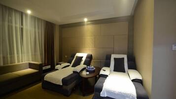 A hotel room with two beds, a sofa, a massage chair, and a small table.