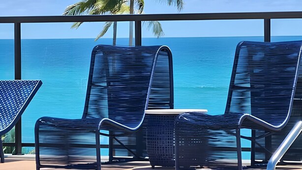 Varanda com duas cadeiras de descanso e uma mesa pequena, com vista para o oceano.