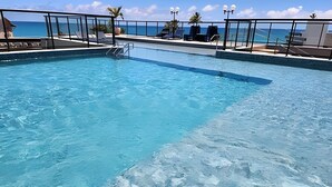 Uma piscina com água azul cristalina, rodeada por espreguiçadeiras e um corrimão.