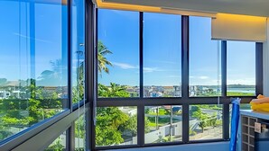 Quarto com grandes janelas que oferecem vista para um horizonte urbano e áreas verdes.