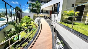 Um edifício moderno com fachada de vidro, uma passarela curva e vegetação ao redor.