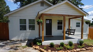 A single-story house with a covered porch, a front door, and a small garden area with rocks and plants. - Cozy Greenville Cottage. Close to downtown! Pet friendly! (Greenville)