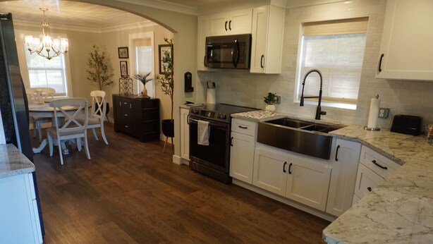 A modern kitchen with white cabinets, stainless steel appliances, and a wooden floor. - Cozy Greenville Cottage. Close to downtown! Pet friendly! (Greenville)